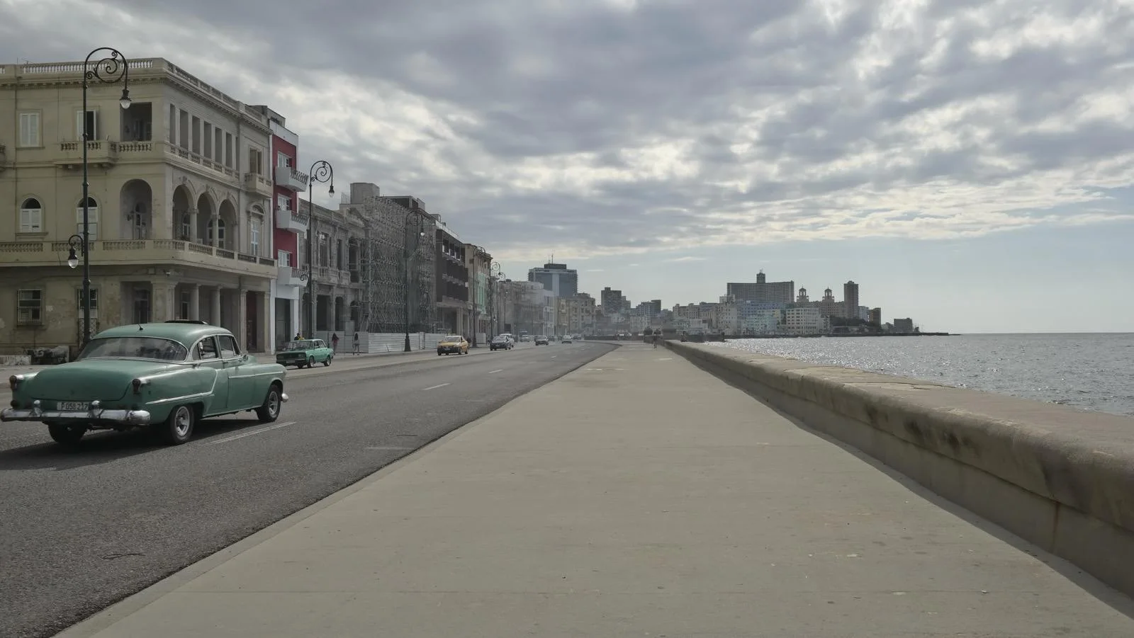 The Malecón in Havana under a grey sky, a mint-green 1950s car driving along the seafront