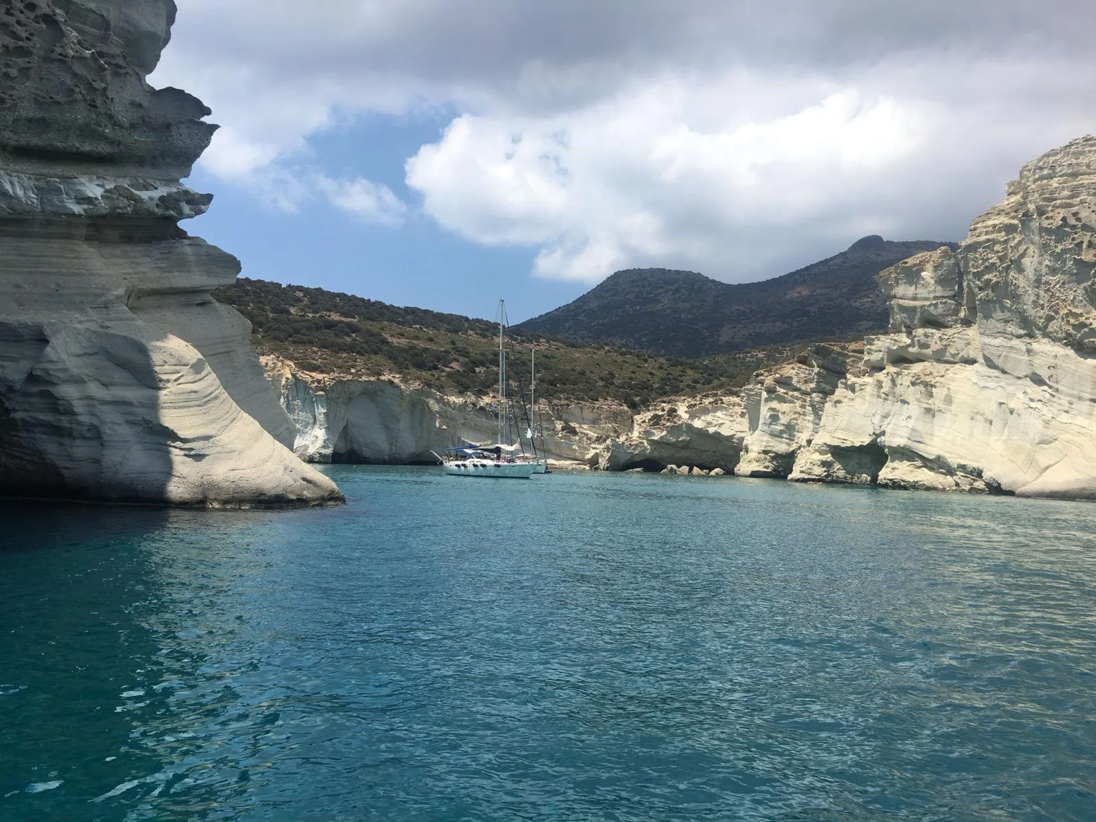 White volcanic cliffs and turquoise water at Kleftiko, a sailing boat moored in the bay