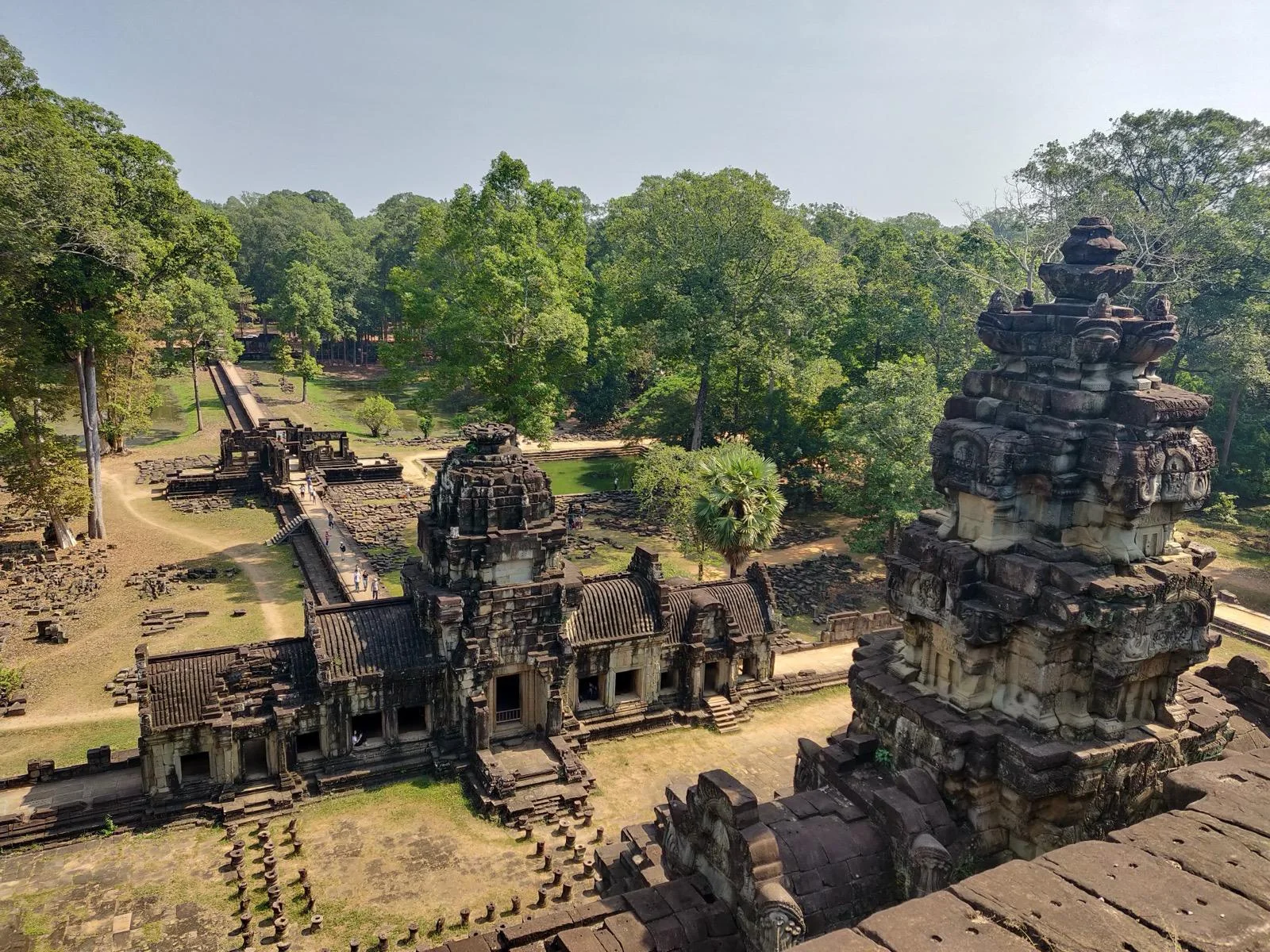 Sandstone towers of a temple in the Angkor complex seen from above, a raised causeway running out through the trees