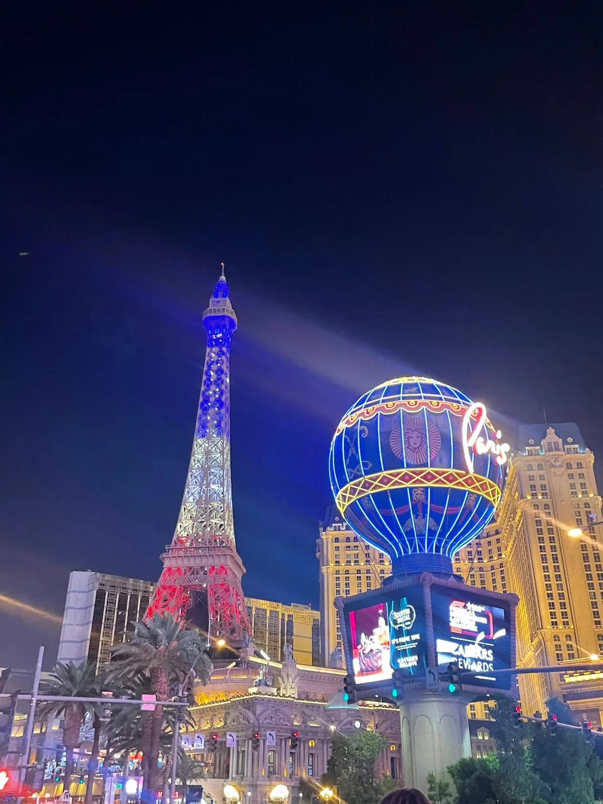 The Las Vegas Strip at night: the Eiffel Tower of Paris Las Vegas lit in blue, white and red, and the hotel's balloon sign